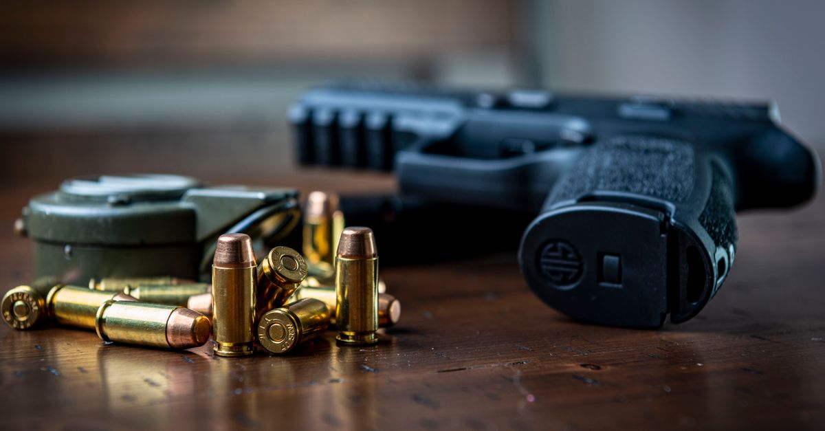 Close view of a handgun with bullets on a wooden surface, emphasizing firearms and ammunition.